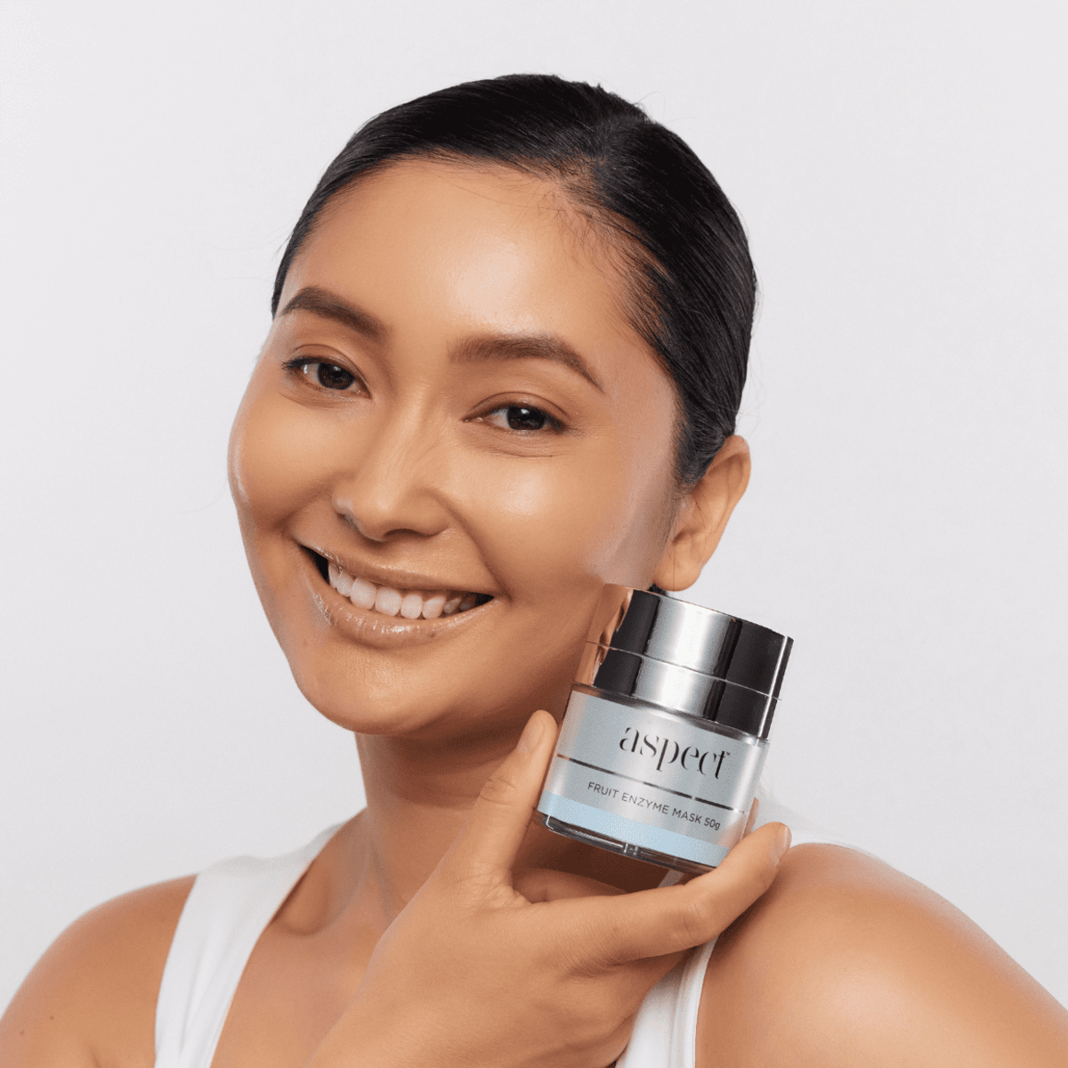 Woman holding Aspect Fruit Enzyme Mask, showcasing the gentle exfoliating fruit enzyme formula designed to brighten and revitalise dull skin.