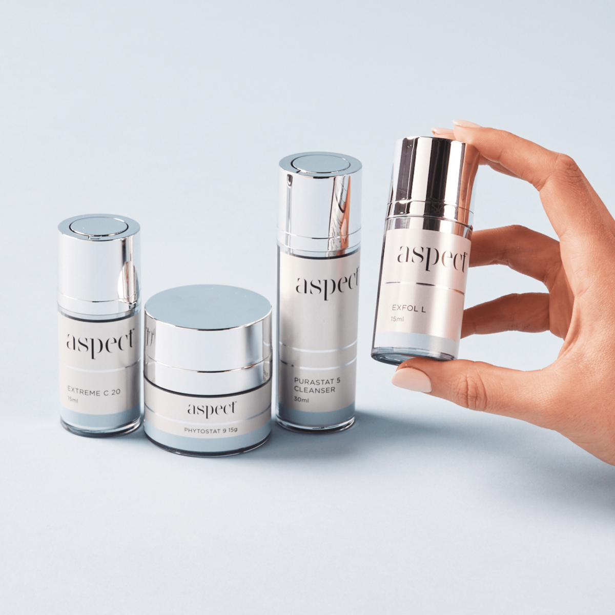 Close-up of the Aspect Starter Kit products with a hand picking up one item, featuring Purastat 5, Extreme C 20, Exfol L and Phytostat 9.