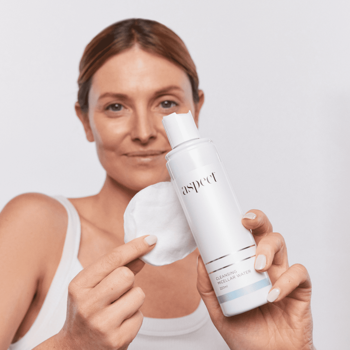 Woman holding Aspect Cleansing Micellar Water with a cotton pad, highlighting its ease of use as a hydrating, sensitive-skin friendly makeup remover.