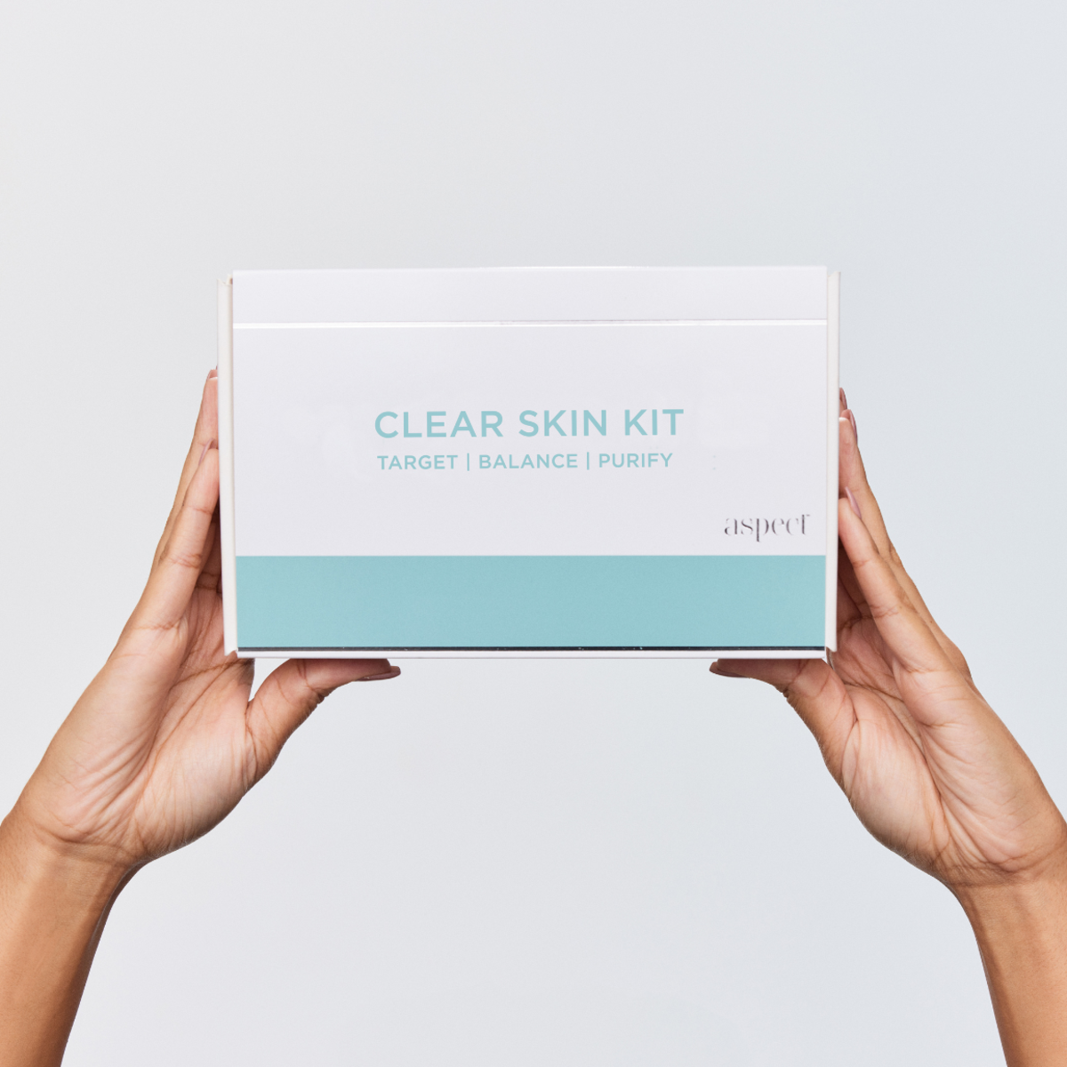 Aspect Clear Skin Kit box held by two hands, showcasing the complete clarifying skincare system for problematic and acne-prone skin.