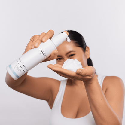 Woman dispensing Aspect Exfoliating Cleanser onto her hand, highlighting its foaming gel texture enriched with AHA and BHA for deep cleansing and skin refinement.