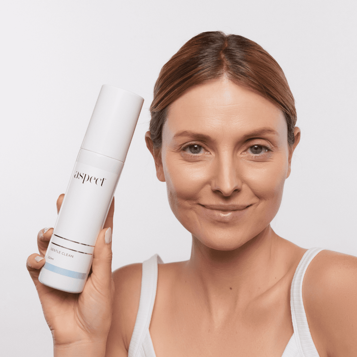 Woman holding Aspect Gentle Clean 220ml gentle foaming gel cleanser, highlighting its soothing, hydrating and lactic acid–infused formula suitable for all skin types.