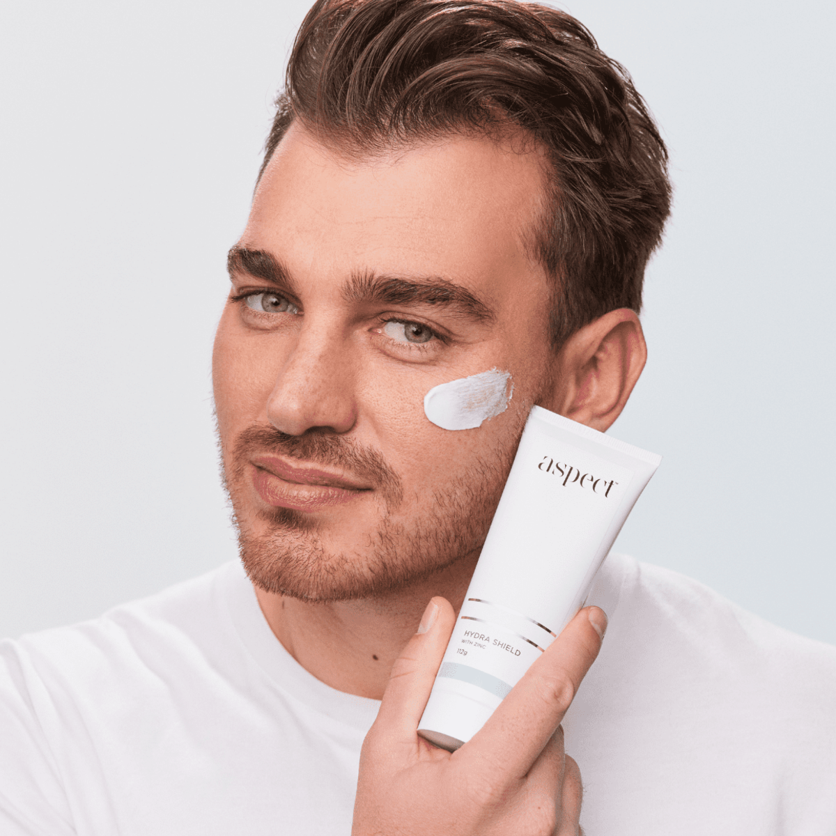 Man holding Aspect Hydra Shield with a visible smear of the moisturiser on his cheek, demonstrating the lightweight hydrating formula that calms and protects skin.