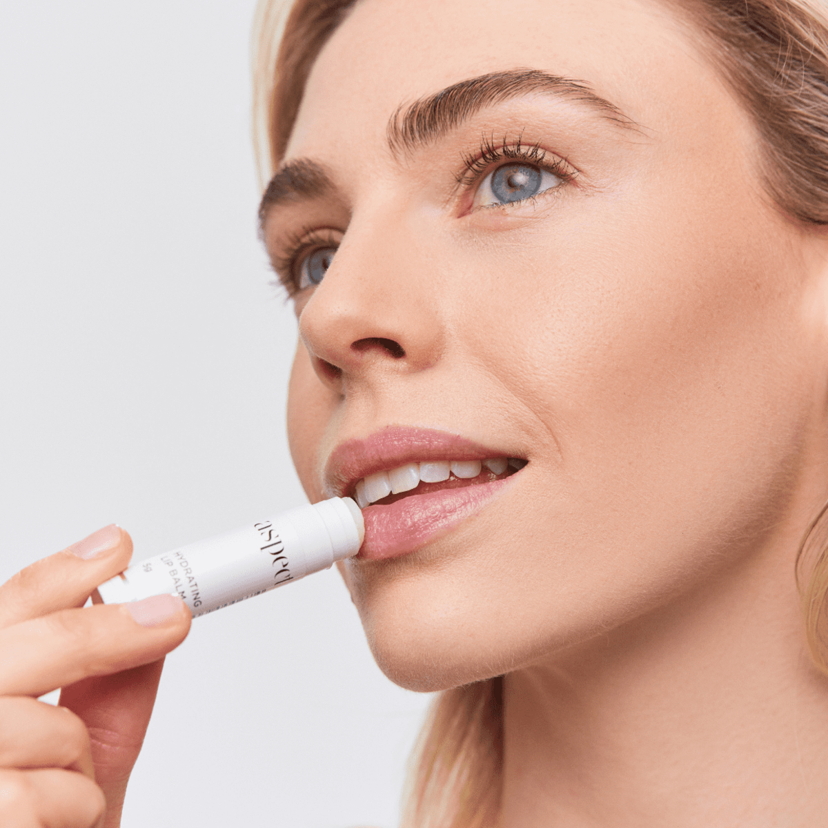 Close-up of a woman applying Aspect Hydrating Lip Balm, showcasing the smooth, nourishing texture designed to hydrate and restore dry lips.