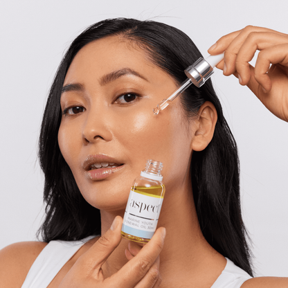 Woman applying Aspect Marine Youth Renewal Oil to her face using the dropper, demonstrating the fast-absorbing marine-infused oil that plumps and smooths skin.