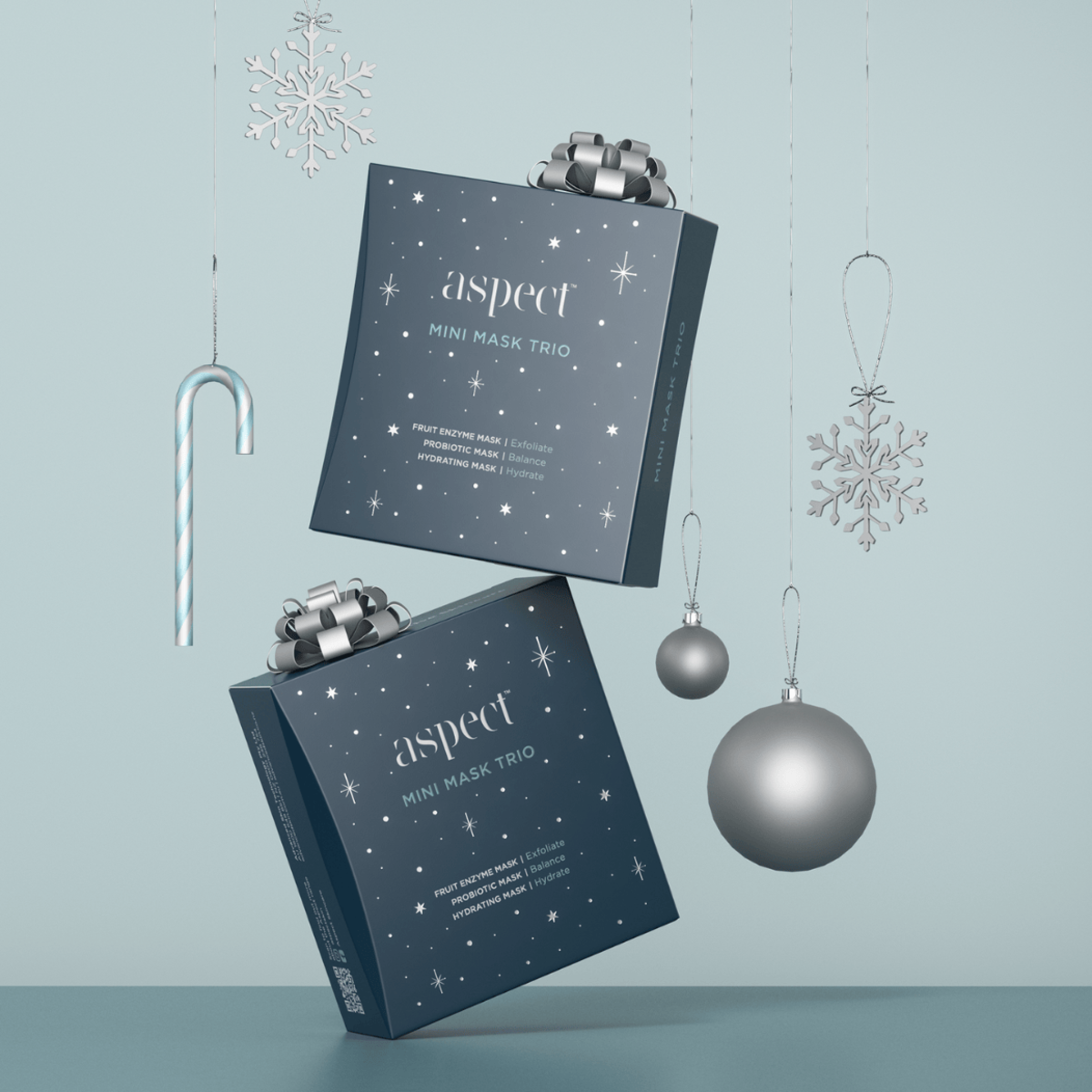 Styled image of two Aspect Mini Mask Trio Limited Edition Kits with silver Christmas decorations, highlighting the skincare set as a luxurious holiday gifting option.