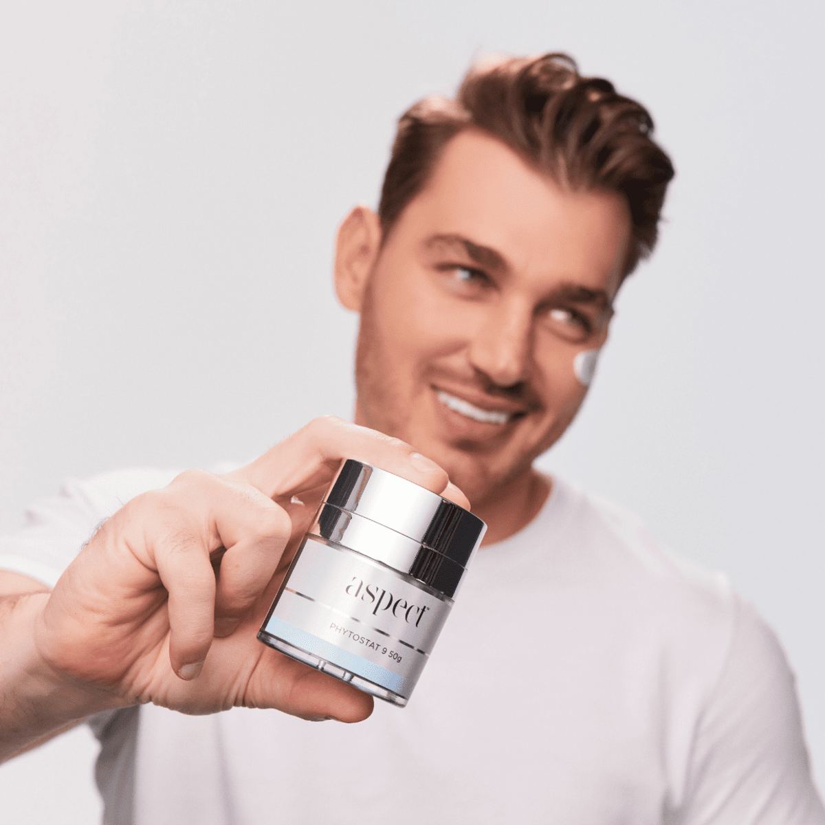 Man holding Aspect Phytostat 9 while wearing the moisturiser on his face, demonstrating the rich, nourishing formula designed to hydrate, firm and replenish skin.