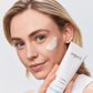 Woman holding Aspect Probiotic Mask with a swipe applied to her cheek, highlighting the creamy probiotic formula that hydrates, softens and calms stressed skin.