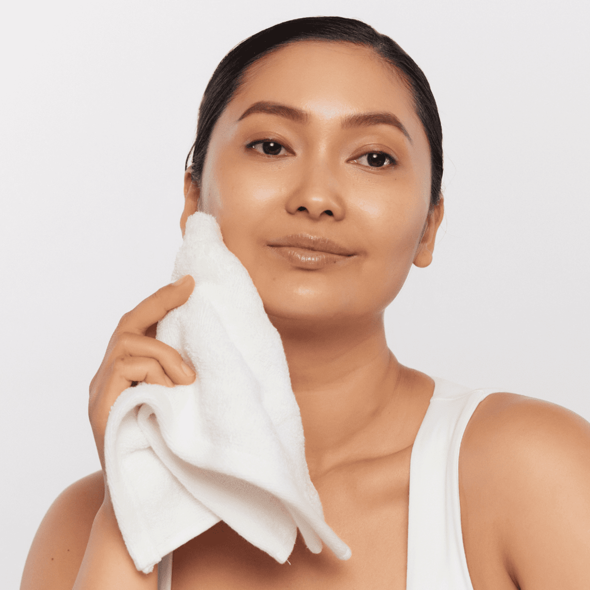 Woman wiping her face with a damp cloth after using Aspect Purastat 5 Cleanser 100ml, demonstrating gentle removal of the exfoliating foaming gel formula.