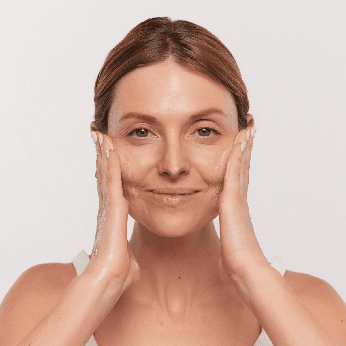 Woman lathering Aspect Purastat 5 Cleanser 220ml to show its silky foaming texture that exfoliates, brightens and deeply cleanses the skin.