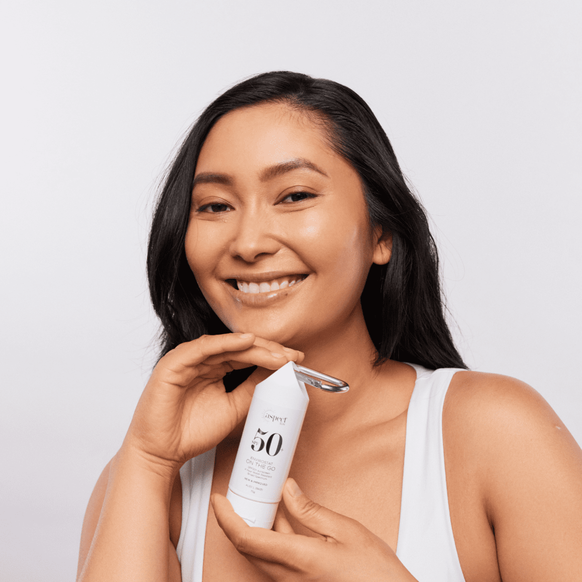 Woman holding Aspect Sun Envirostat ‘On The Go’ SPF50+ sunscreen tube, demonstrating compact travel-friendly size and easy daily use.